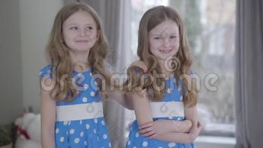 笑容满面的黑发白种人双胞胎姐妹穿着类似<strong>点缀</strong>的蓝色连衣裙在家里摆姿势。 积极的<strong>小</strong>妹妹